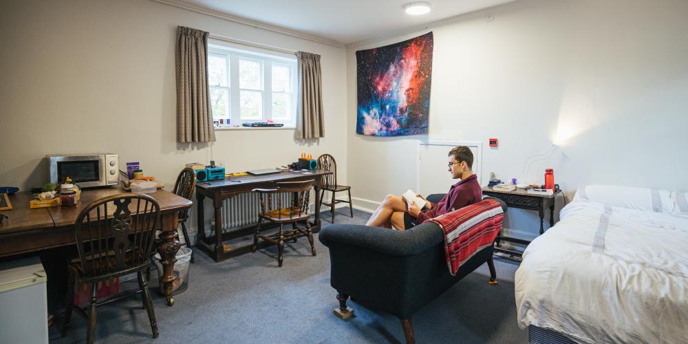 An student sits reading on the couch in a postgraduate room on Trinity's main site.