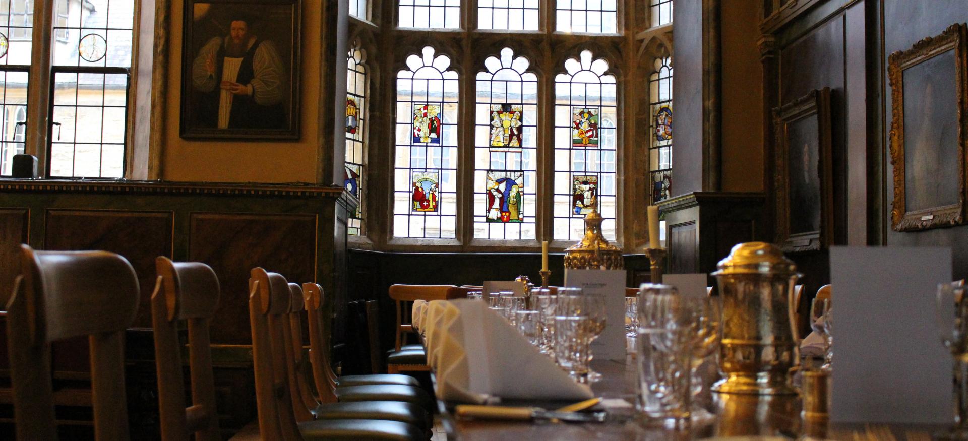 Trinity dining hall set for dinner with stained glass windows in background