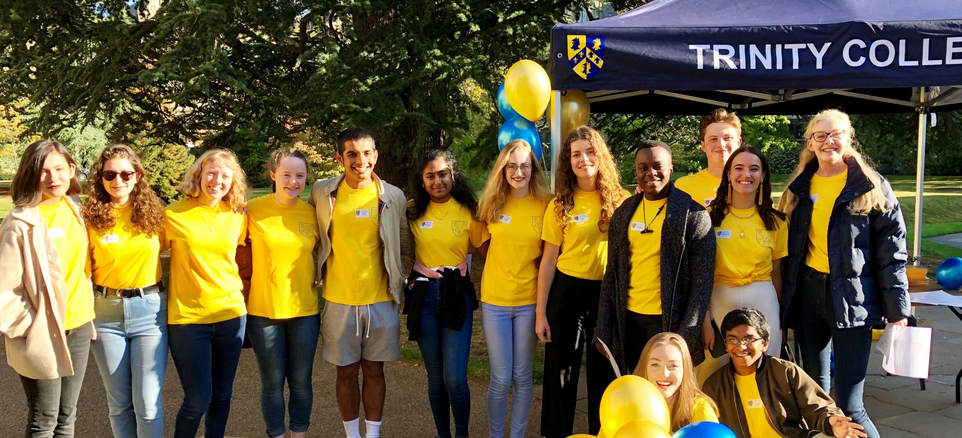 A group of Trinity College student ambassadors stands in front of a marquee at Open days.
