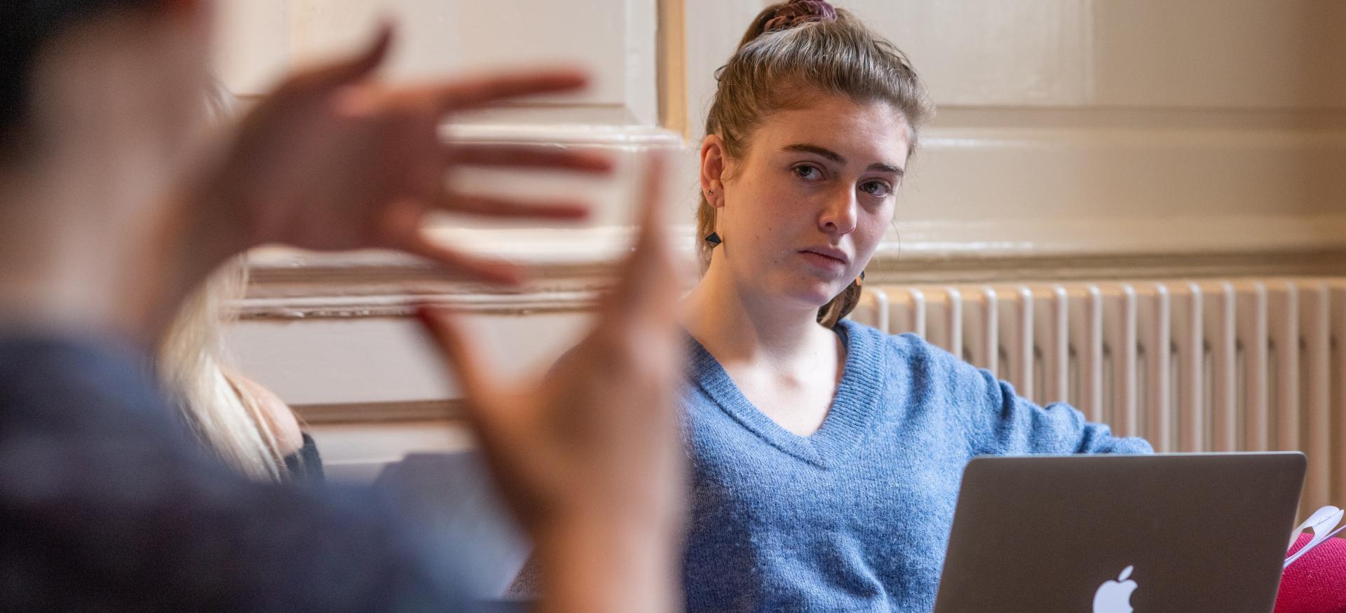 A tutor's hands gesture out of focus in the foreground while a student looks in concentration in the background.