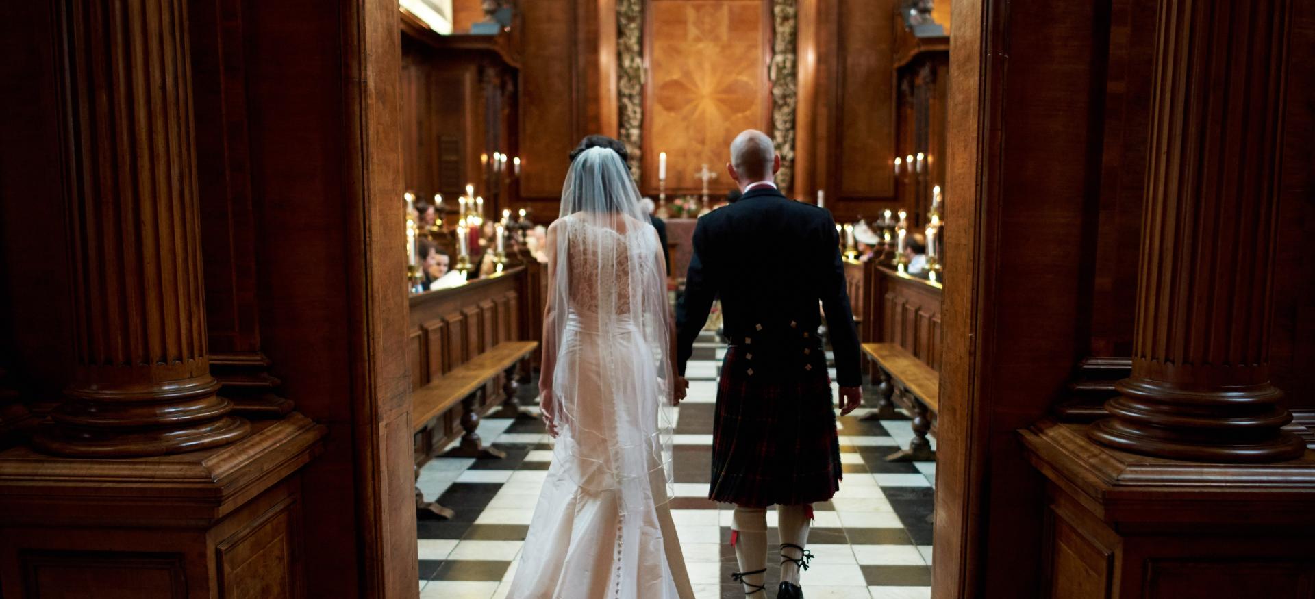 A bride and groom walk into the Trinity College chapel during a wedding service. 