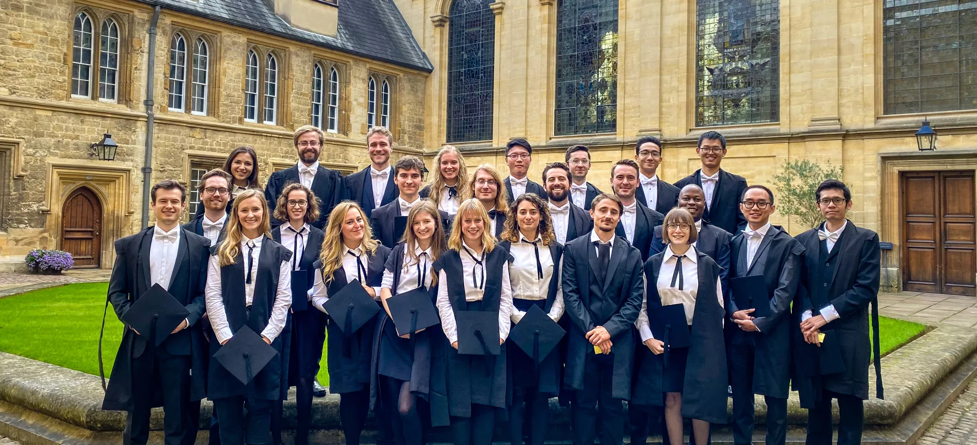 A group of MCR freshers stands wearing university sub-fusc before their matriculation in the college's Durham Quad.