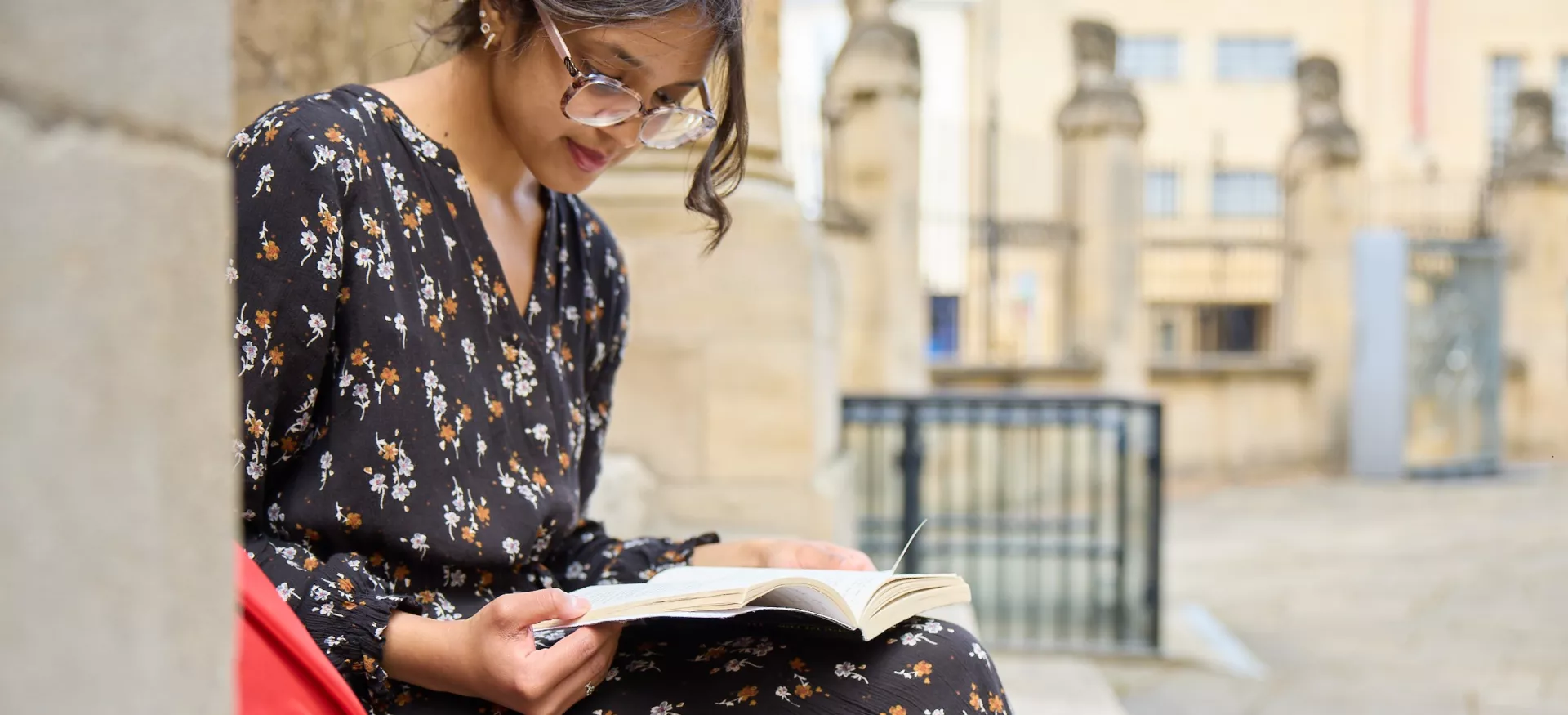 A young Asian woman sits on the steps outside the Radcliffe Camera reading.