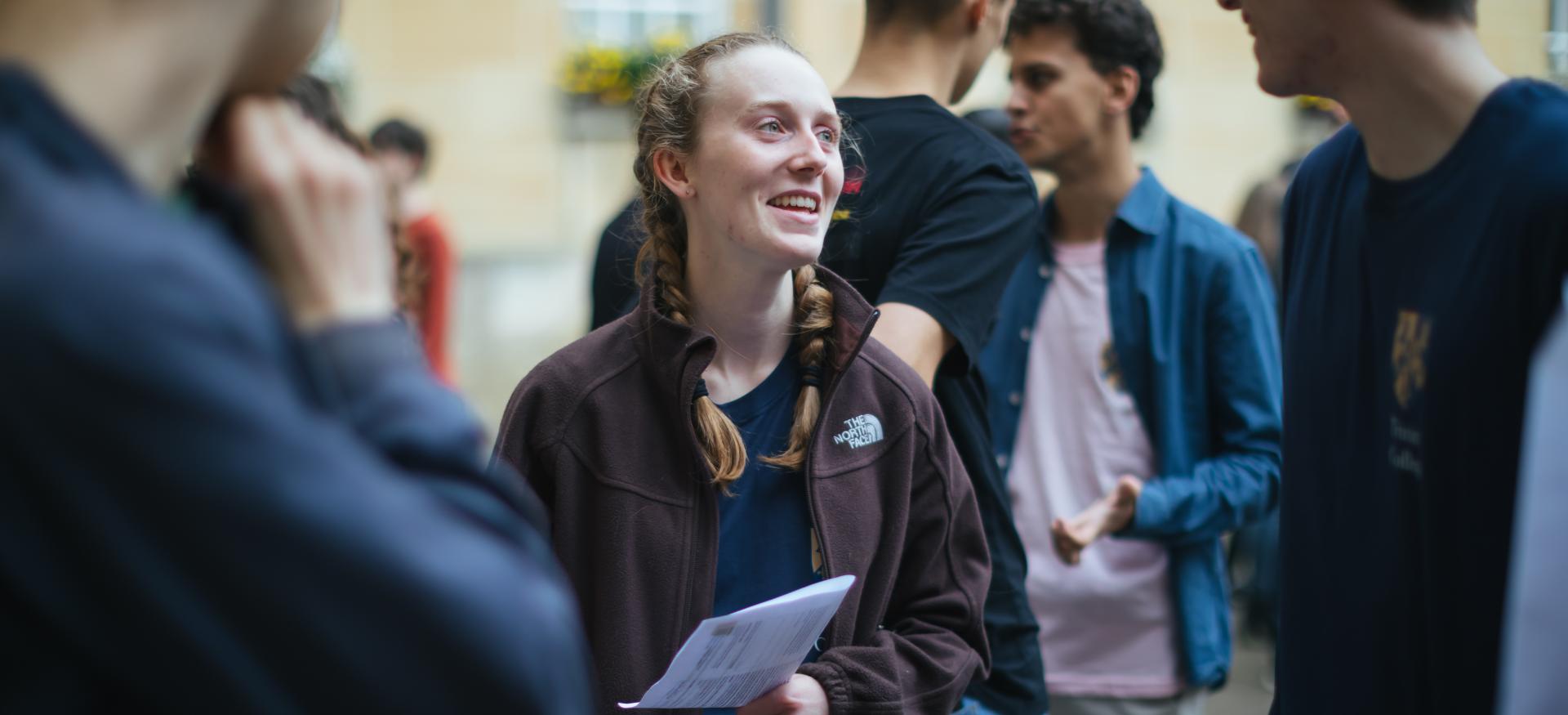 A female student smiles while gesturing to other students during open days.