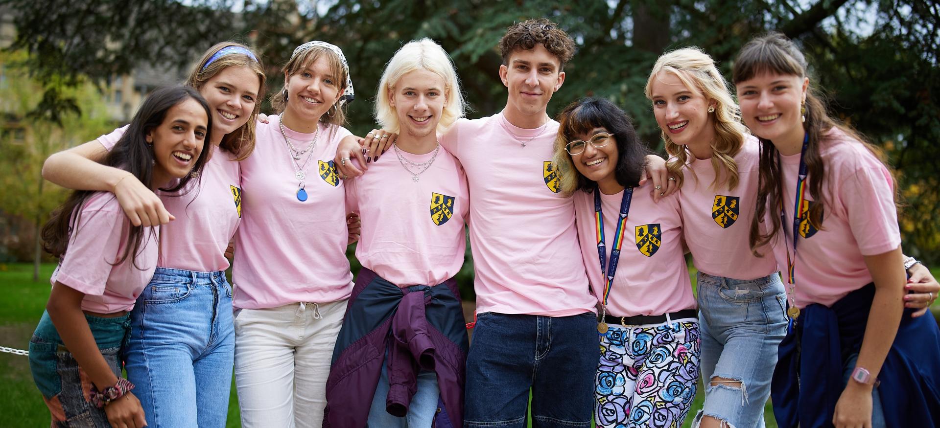 A group of trinity JCR freshers reps stand with their arms around each other smiling. They are wearing matching pink shirts.
