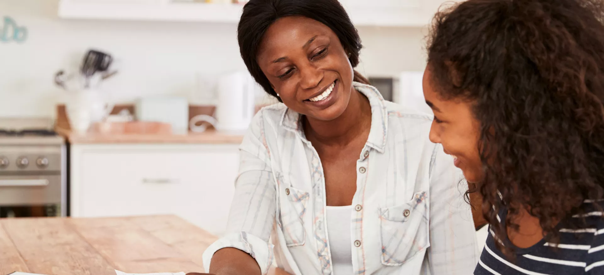 A mother sits with her daughter as she looks at something on a screen device.