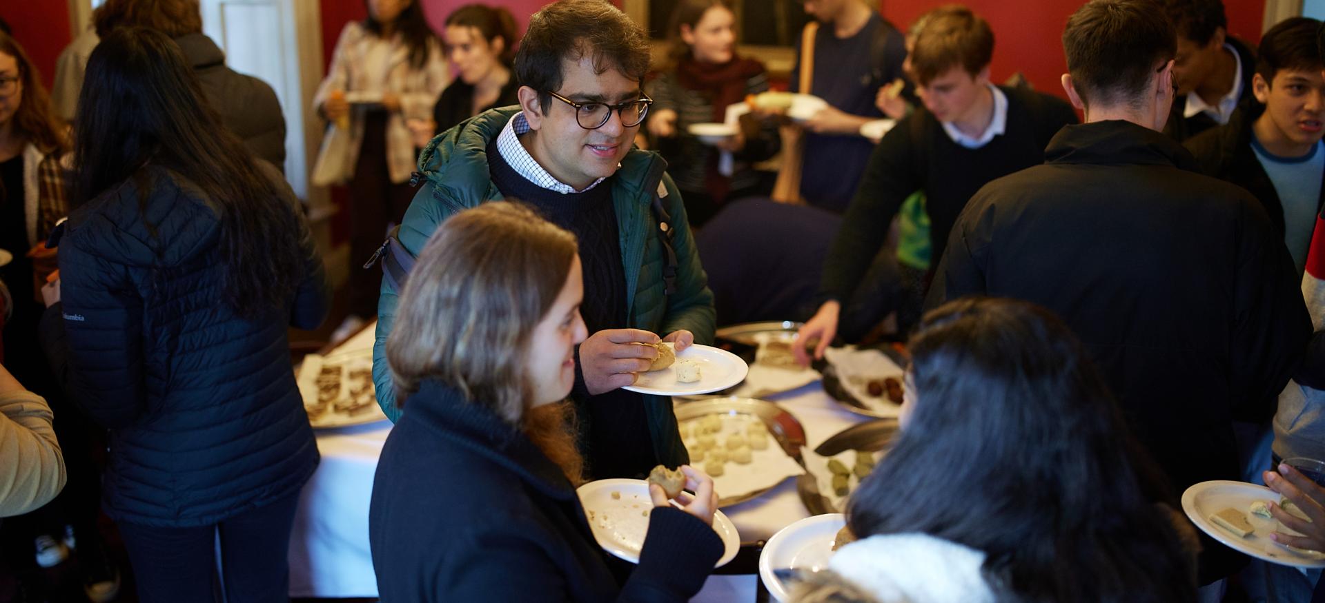 A group of postgraduate students take plates of food and chat in the President's Lodgings of Trinity College.