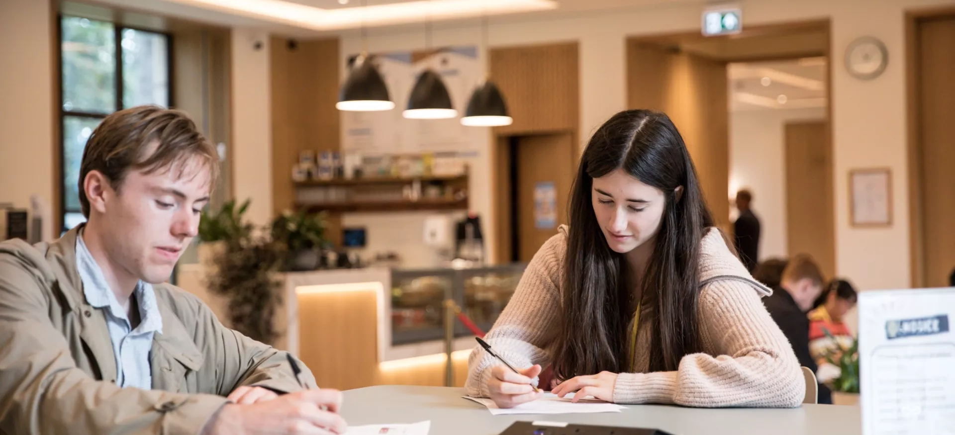 A male and female student work at a table in Trinity's cafe.