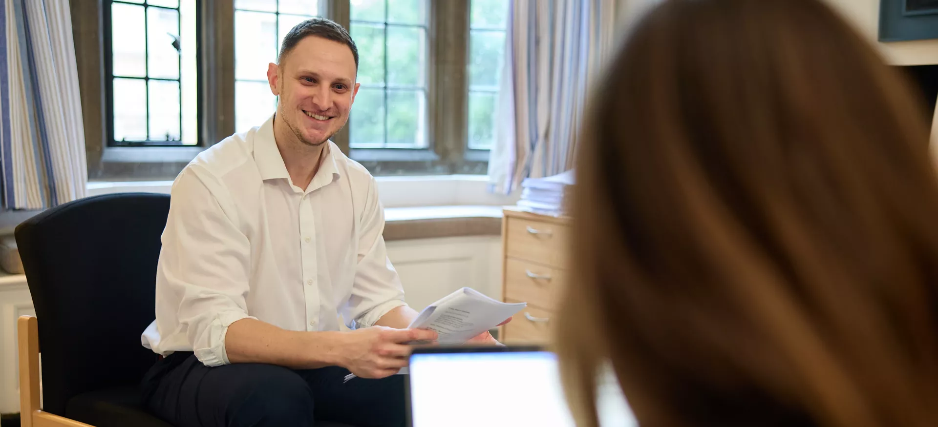 Trinity tutor Luke Rostill sits smiling in a tutorial.