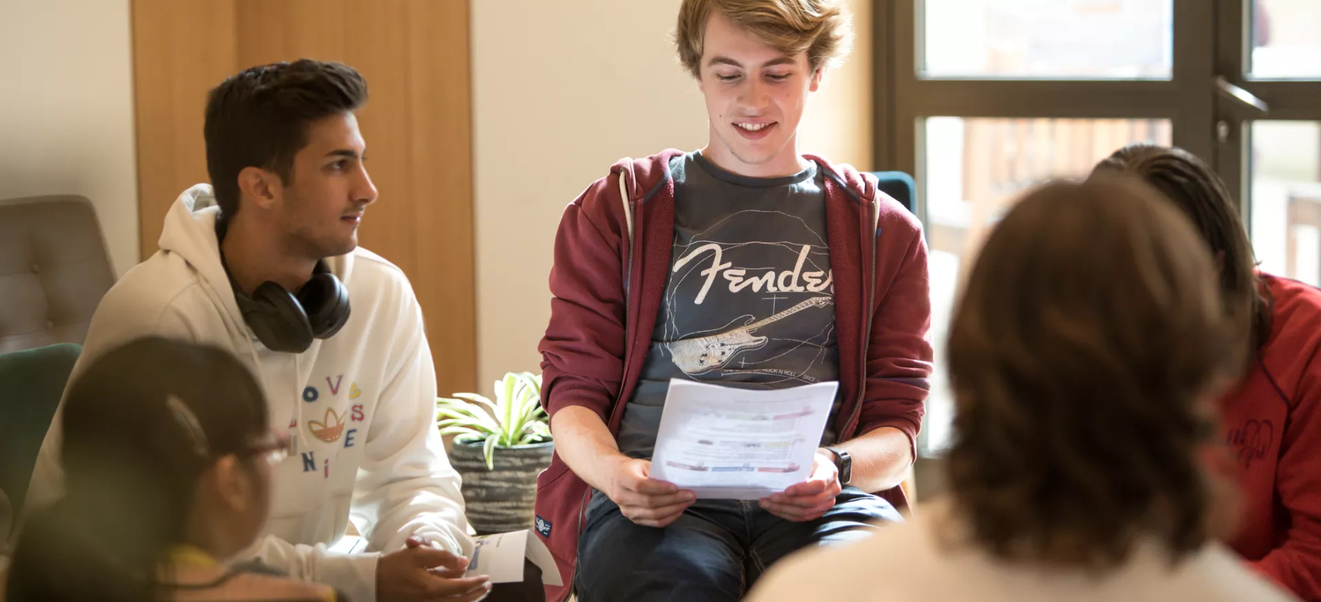 A group of students sit in the cafe at Trinity; one student is looking at a paper with questions on it.