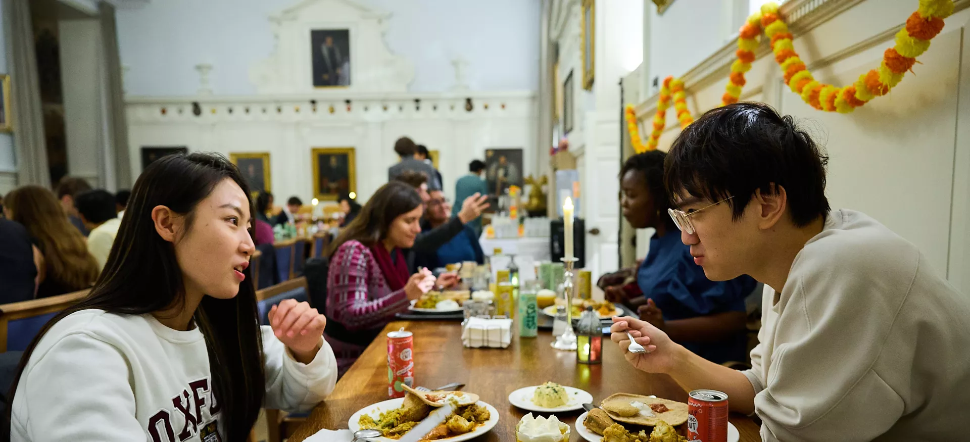 A group of students sit in the Trinity Dining hall eating during the Diwali themed meal in college.