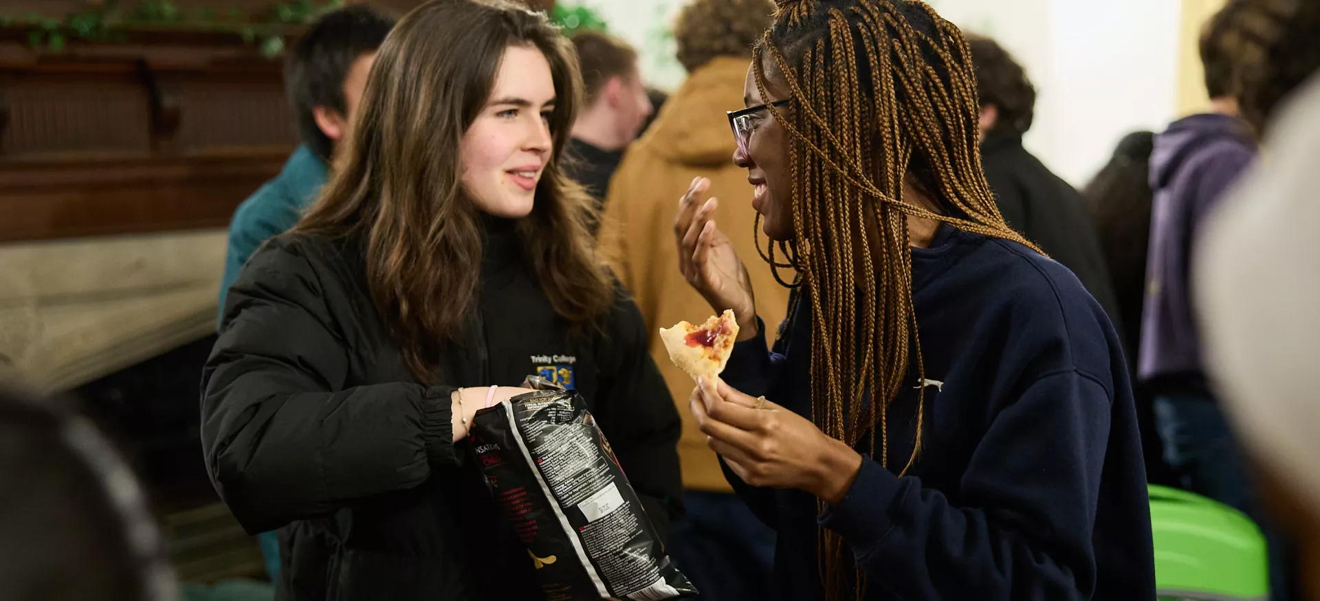 Two female students chat over snacks in the Trinity JCR. 