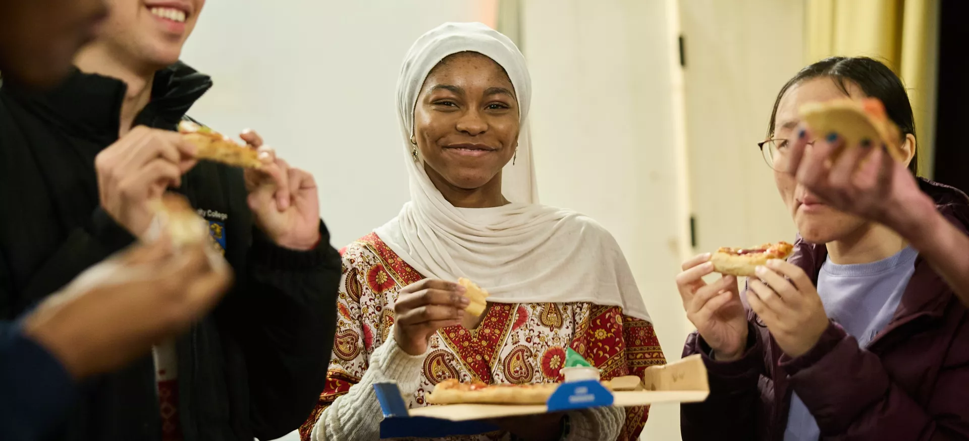 Students stand in the Trinity JCR holding pizza slices at a JCR pizza night.