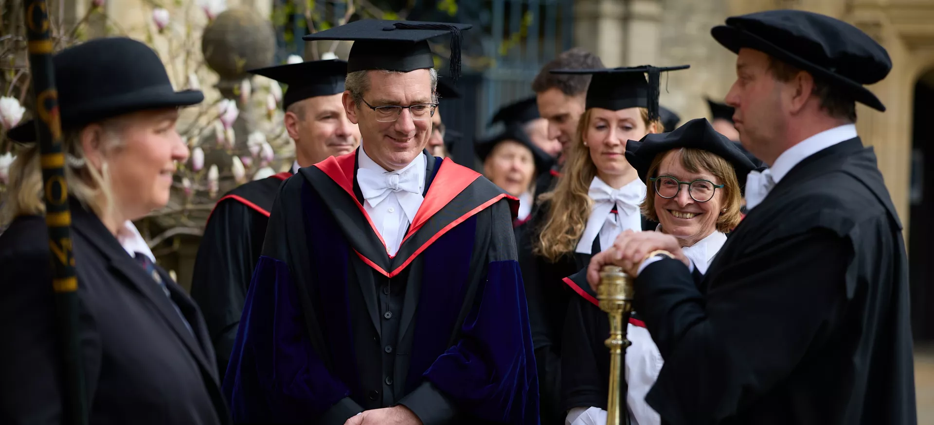 Trinity Fellow Nick Barber stands in a gown and cap with other members of college preparing for the ceremony to admit him as Senior Proctor.