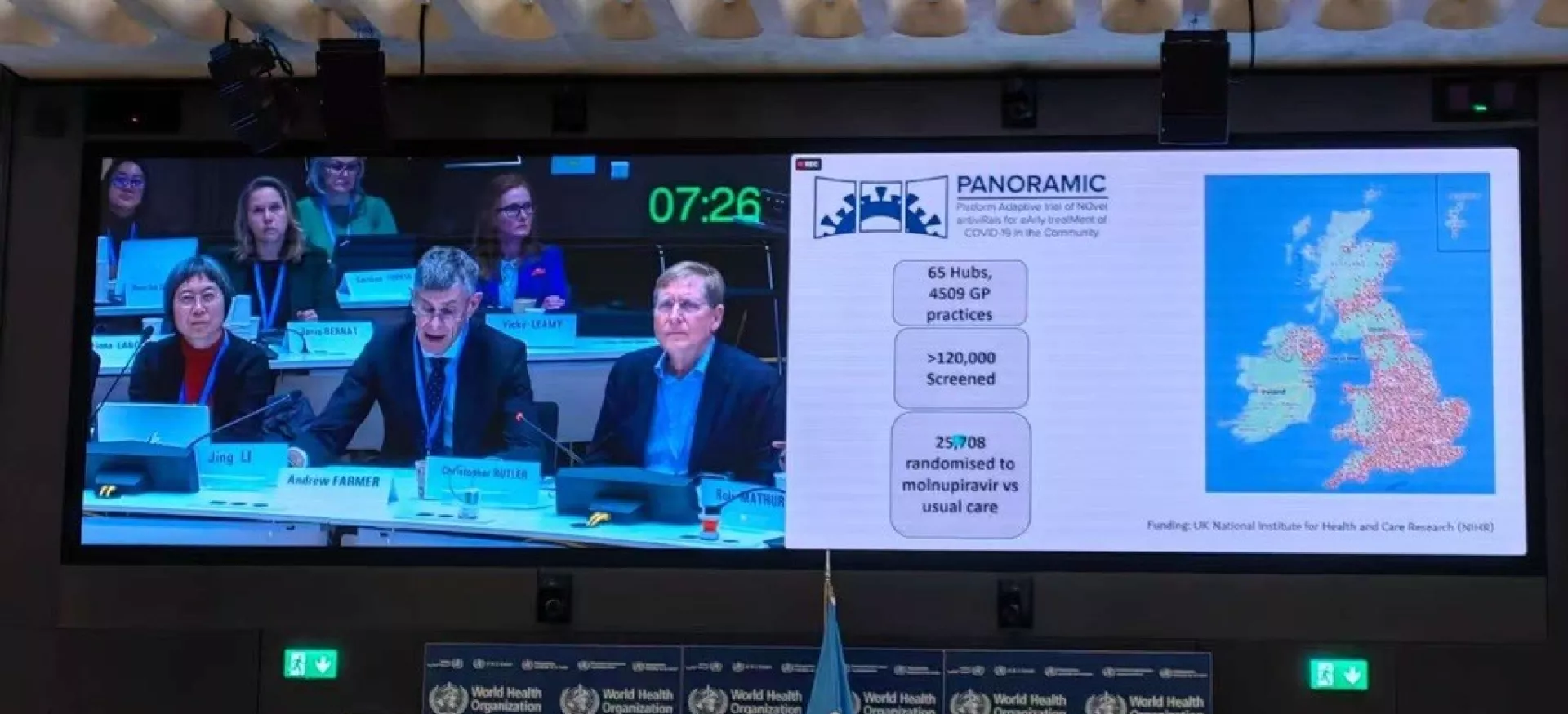 Christopher Butler sits in a session at the World Health Organisation showing slides on a screen about the PANORAMIC covid-19 trial.