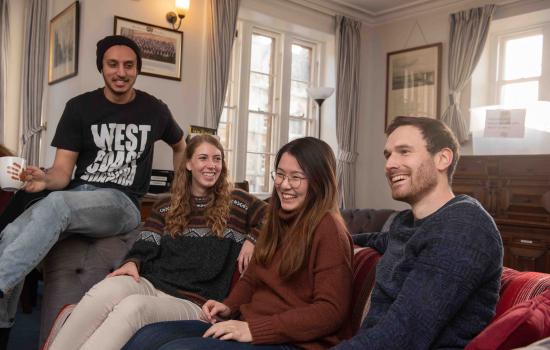 A group of four male and female postgraduate students sit on a couch laughing.