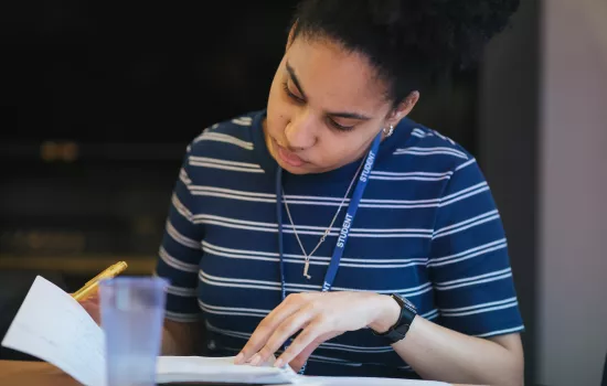 A female student consults a book while studying at a desk.