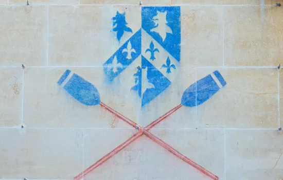 A chalked image of the Trinity College shield with boat club blades on the wall of a college building.