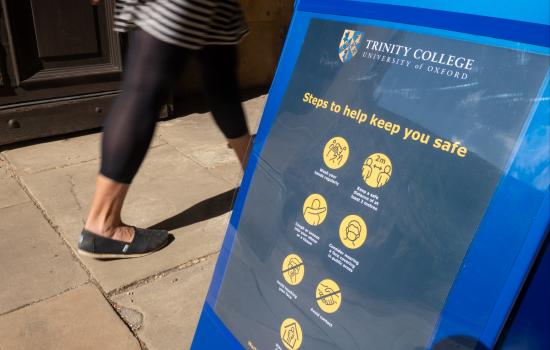 A woman's legs in motion walk past a sign saying 'Trinity College: steps to help keep you safe'