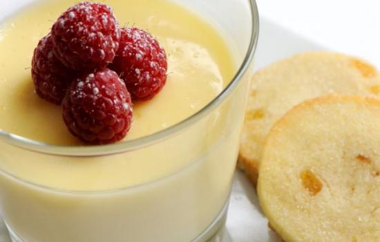 A glass of lemon posset with shortbread rounds on a plate next to it.