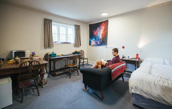 An student sits reading on the couch in a postgraduate room on Trinity's main site.