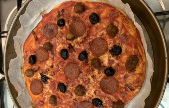 A home cooked pizza on a pan with pepperoni and olives.