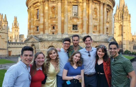 A group of Trinity postgraduates stands in front of the Radcliffe Camera in Oxford.