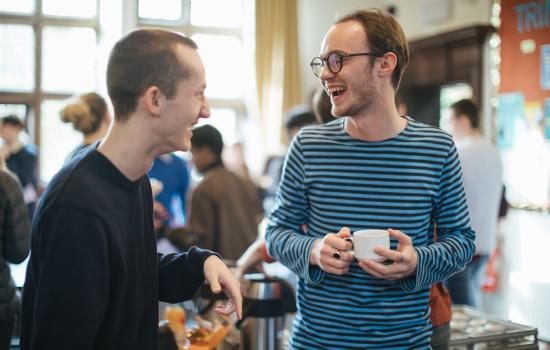 Two male students laugh during conversation at a Trinity welfare tea.