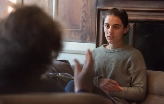 A female student sits in a tutorial; in the foreground but out of focus is the back of a tutor's head, gesturing.