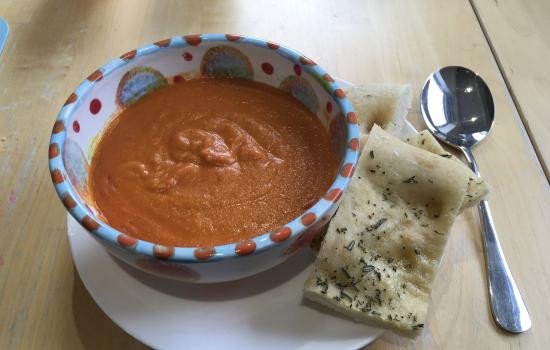 A bowl of tomato soup on a plate with a slice of focaccia bread. 