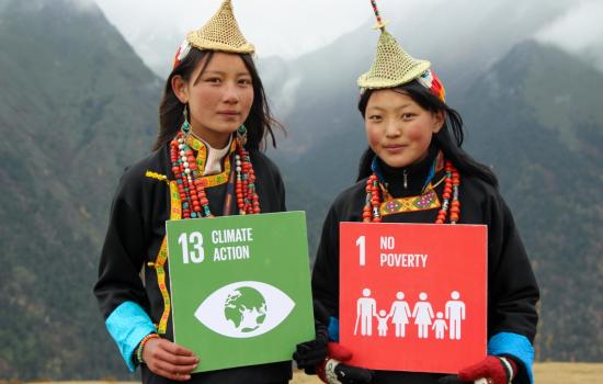 Two girls in Bhutan hold up signs saying 'climate action' and 'no poverty'.