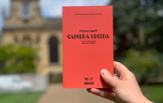 A hand holds up a copy of Camera Lucida in Ukrainian in front of the Trinity College chapel.
