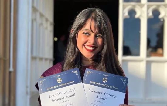 Rai Sengupta stands holding two awards from the Weidenfeld-Hoffmann Trust.