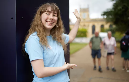 A student stands at the front gate of Trinity college welcoming visitors in.
