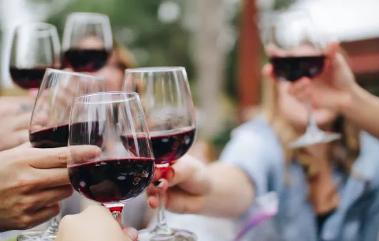 People hold red wine glasses together to cheers 