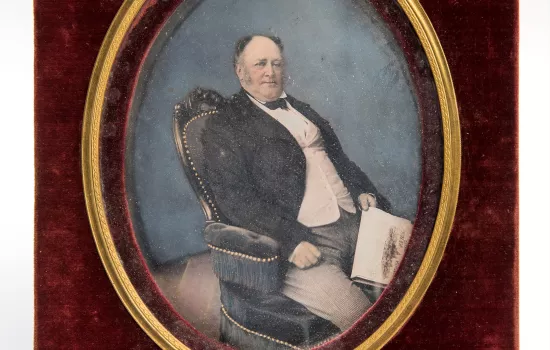 A hand-painted half-plate daguerreotype in green leather case of Seated man holding a copy of the Illustrated London News, c. 1850 