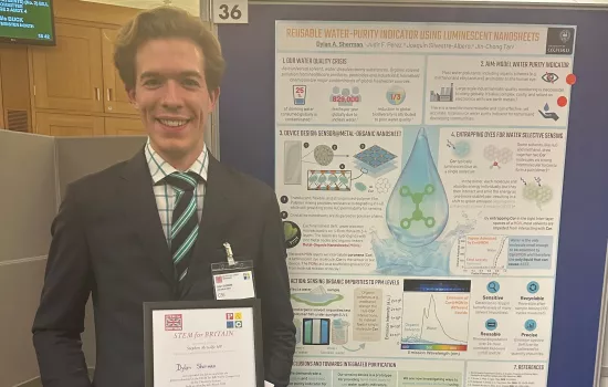 Dylan Sherman stands at the STEM for Britain event in front of his prize-winning poster. He holds his medal citation.