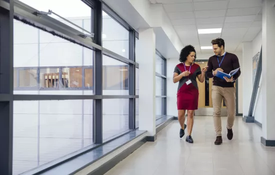 Two teachers walk down a school hallway chatting.