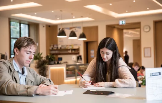 A male and female student work at a table in Trinity's cafe.