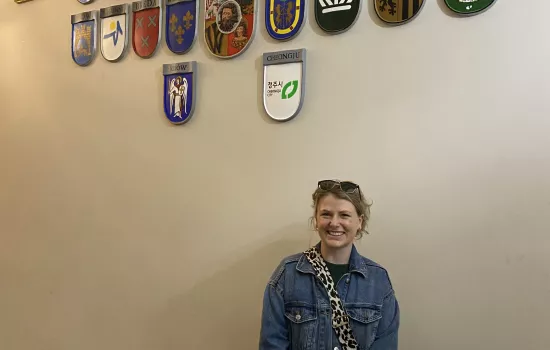 Trinity student Ishbel Henderson stands in a building with a bunch of European country shields on the wall.