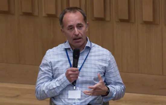 Tom Drew sits with a microphone talking.