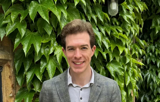 Dylan Sherman stands holding a certificate confirming he won the Three-Minute Thesis competition at Oxford.