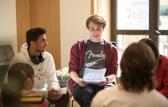 A group of students sit in the cafe at Trinity; one student is looking at a paper with questions on it.