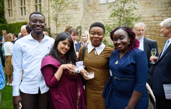 Four trinity postgraduates pose at a reception in the college President's Garden.
