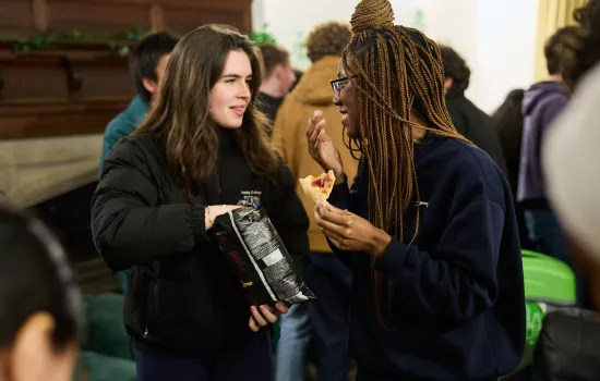 Two female students chat over snacks in the Trinity JCR. 