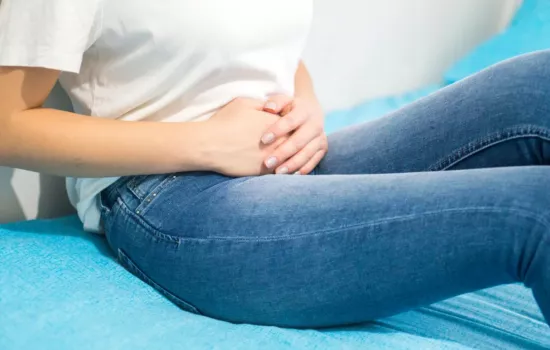 A woman holds her midsection while sitting on a blue couch.