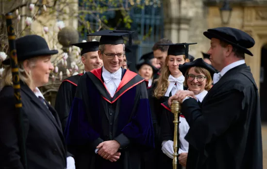 Trinity Fellow Nick Barber stands in a gown and cap with other members of college preparing for the ceremony to admit him as Senior Proctor.