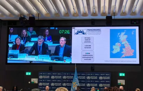 Christopher Butler sits in a session at the World Health Organisation showing slides on a screen about the PANORAMIC covid-19 trial.