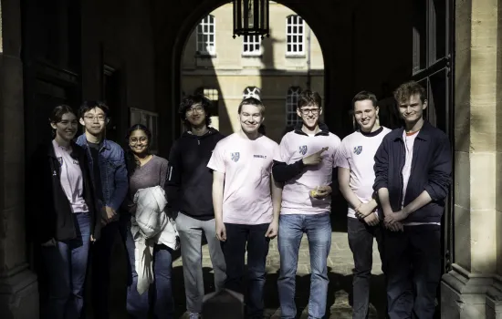 A group of Trinity undergraduates in pink shirts stand in the college's chapel archway on moving-in day. 