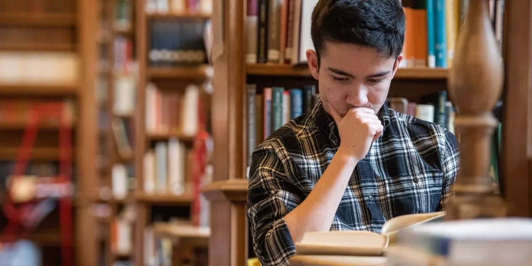 A student sits in the Trinity Library studying with rows of books behind him.
